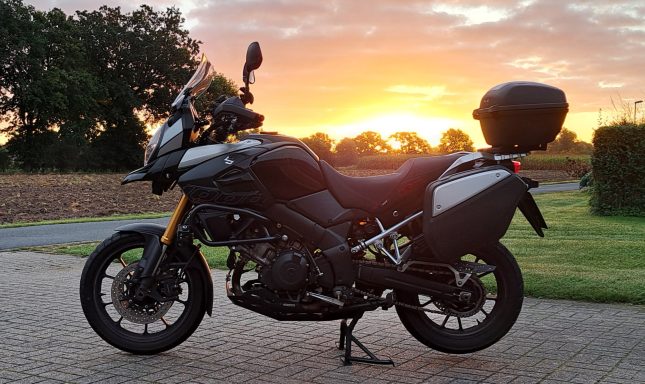 Schwarzes Motorrad mit Koffer vor einem Sonnenuntergang auf einer Wiese.